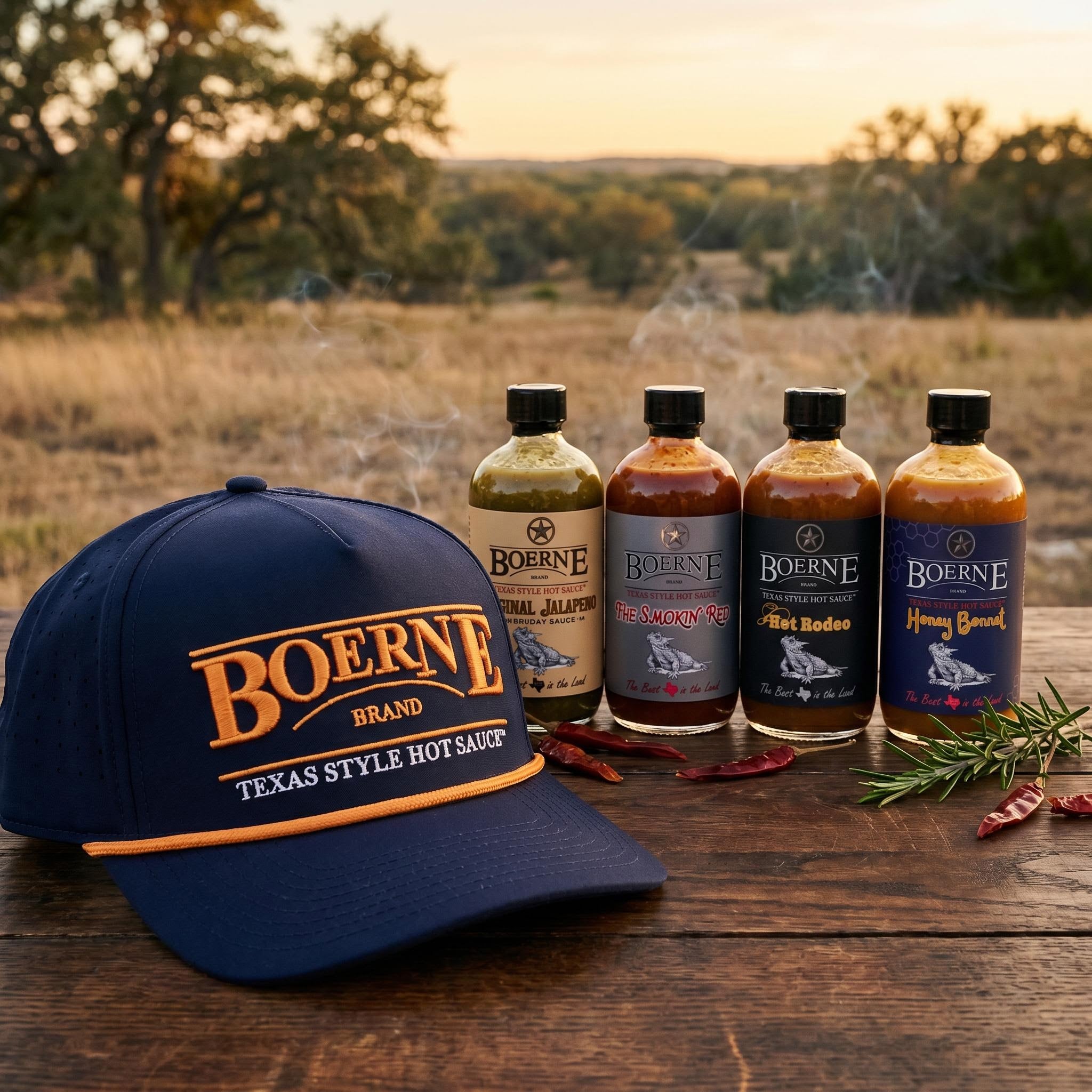 Texas Gift Box - Navy Rope Performance hat in close foreground with four Boerne Brand hot sauce bottles behind, realistic proportions, Texas hill country background